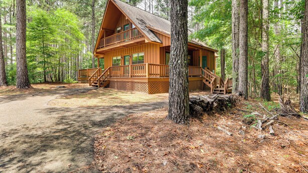 A cabin with a balcony and a porch, surrounded by tall trees. - Pickwick Lake Cabin w/ Private Marina Access (Iuka)