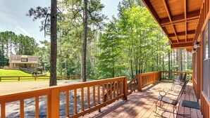 A wooden deck with a railing, overlooking a forested area with a cabin in the background. - Pickwick Lake Cabin w/ Private Marina Access (Iuka)