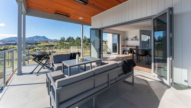 Un patio extérieur moderne avec un plafond en bois, un canapé, une table et un barbecue.