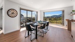 Un vaste espace dédié à la salle à manger, avec une grande table et des chaises, une horloge au mur et une vue sur un paysage grâce à de grandes fenêtres.
