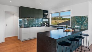 Une cuisine moderne dotée d’un grand îlot central, de meubles blancs et offrant une vue sur un paysage verdoyant grâce à une grande fenêtre.