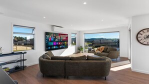 Un salon moderne doté d’un grand téléviseur à écran plat, d’un canapé confortable et offrant une vue sur l’extérieur grâce à de grandes fenêtres.