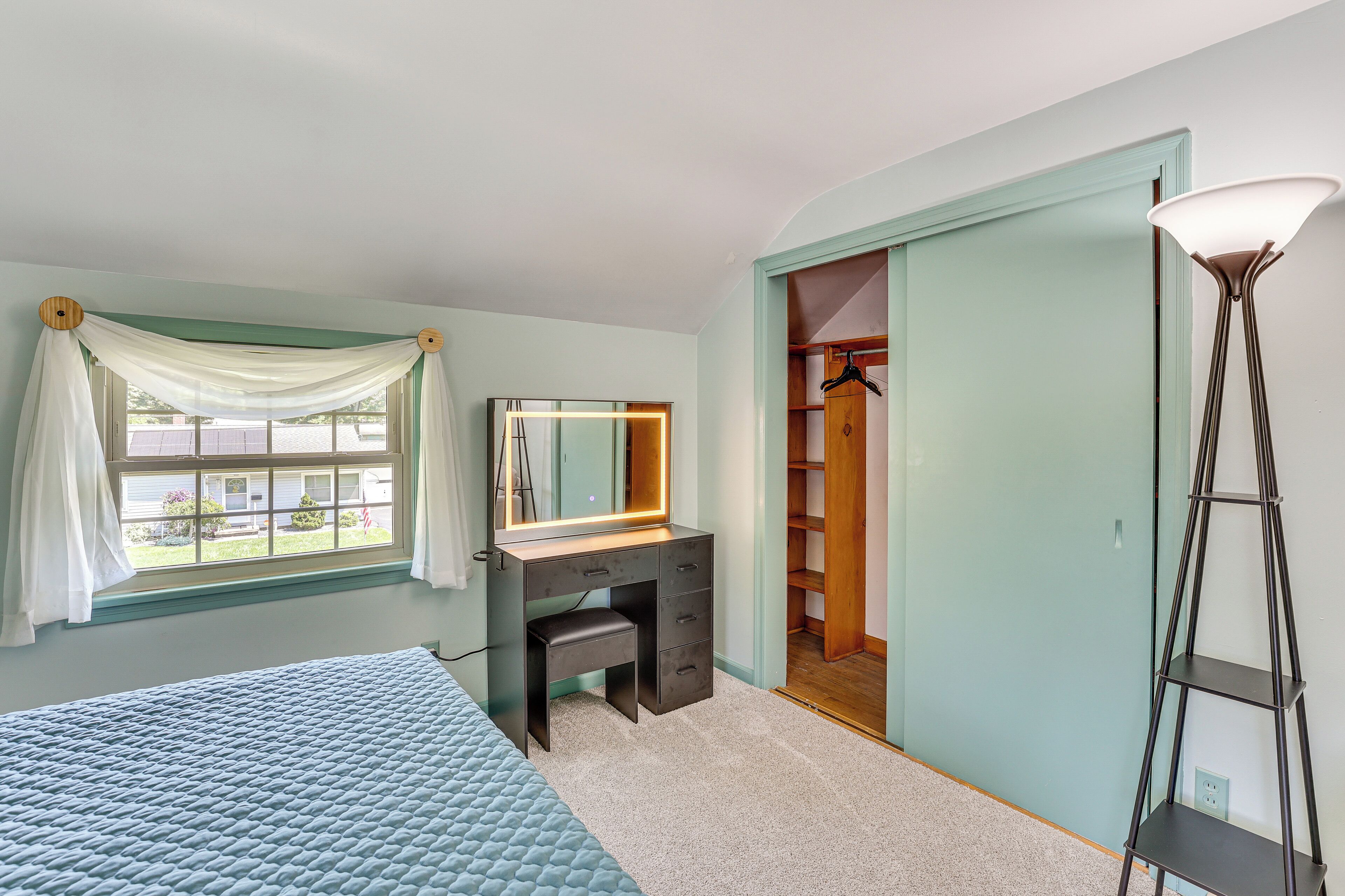 A bedroom with a bed, a vanity with a mirror, a walk-in closet, and a floor lamp.