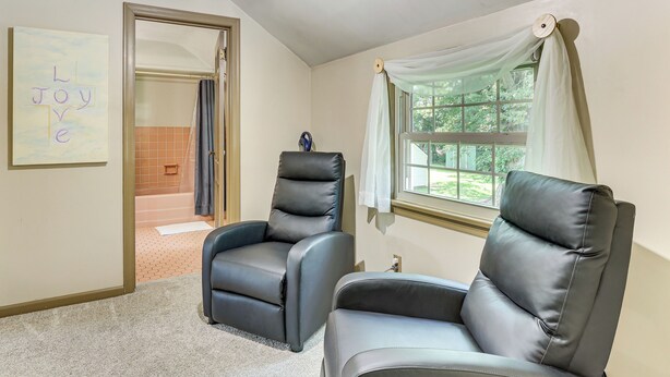 Una habitación con dos sillones de cuero reclinables, una puerta que da al baño y una ventana con cortinas.