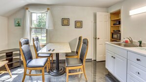 Un comedor con una mesa y sillas, una ventana con cortinas y una cocina con armarios blancos y un lavamanos.