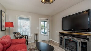 A living room with a red sofa, a black table, a flat-screen TV, a fireplace, and a door leading outside. - Hallelujah Acres Side 2 (Georgetown)