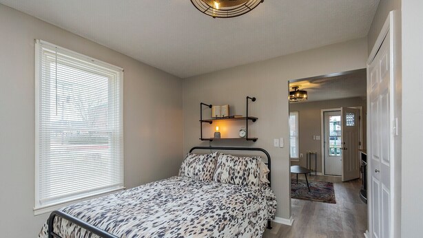 A bedroom with a bed, a window with blinds, a bedside table, a lamp, and a door leading to another room. - Hallelujah Acres Side 2 (Georgetown)