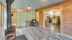 A rustic interior with a wooden floor, a black leather chair, a kitchen area, and a visible clock. - Pond & Fire Pit: Charming Log Cabin near Blue Rock (Philo)