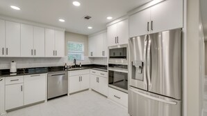 Una cocina moderna con electrodomésticos de acero inoxidable, armarios blancos y una encimera negra.