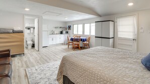 A bedroom with a large bed, a wooden chair, a small table, and a view of the kitchen and bathroom. - Walk to Norfork Lake: Guest House in Henderson (Henderson)