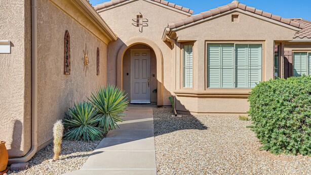 Une maison à l’extérieur beige, avec une porte blanche et un petit jardin agrémenté d’un cactus et d’un arbuste.