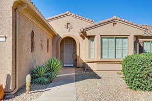 A house with a beige exterior, a white door, and a small garden with a cactus and a bush. - Step-Free, Sun City Grand Home w/ Resort Amenities (Surprise)