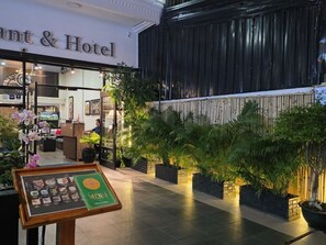 A hotel lobby with a reception desk, a menu stand, and a plant-lined walkway. - Milan Restaurant & Hotel (Phnom Penh)