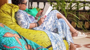 A person sitting on a sofa with a book, surrounded by colorful cushions and a painting on the wall. - Eagle View Golf (Kigali)