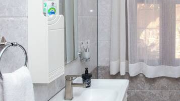 Un baño con lavamanos blanco, espejo y toallero.