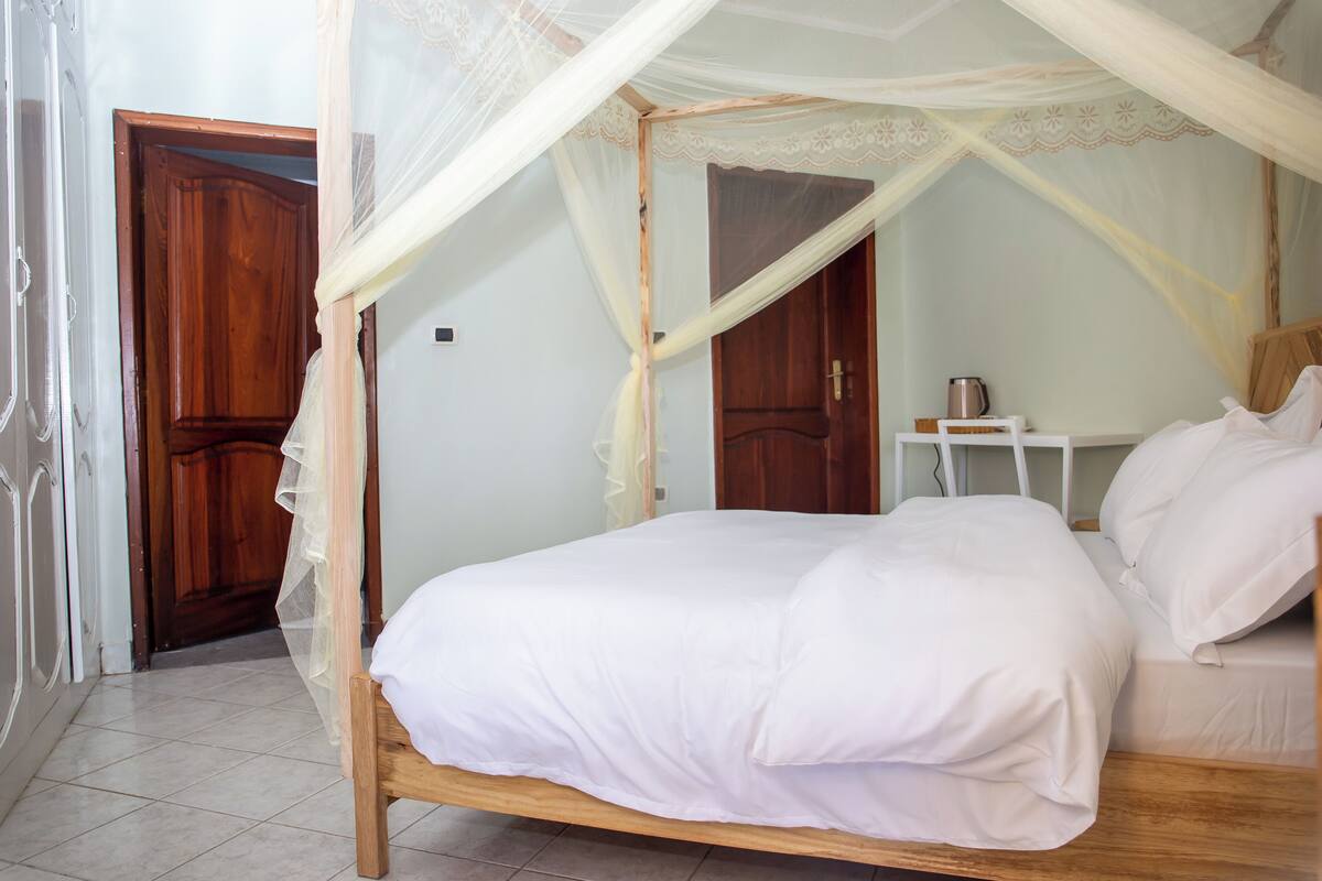 A bedroom with a wooden bed, white bedding, a nightstand, and a wooden wardrobe.