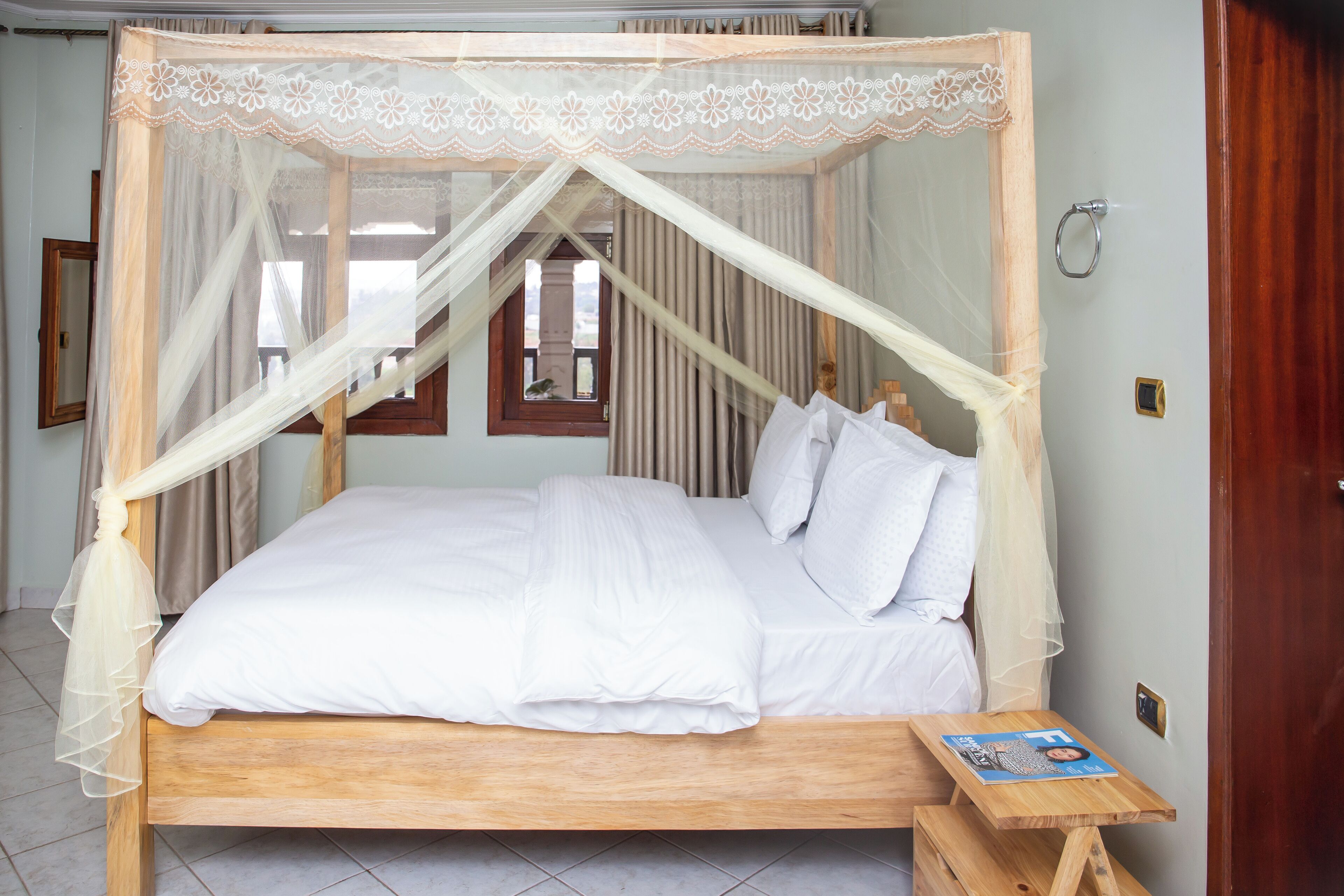 A four-poster bed with white linens, a wooden headboard, and a wooden bedside table with a magazine.
