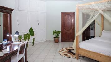 A bedroom with a wooden bed, a desk with a chair, a potted plant, a wardrobe, and a door.