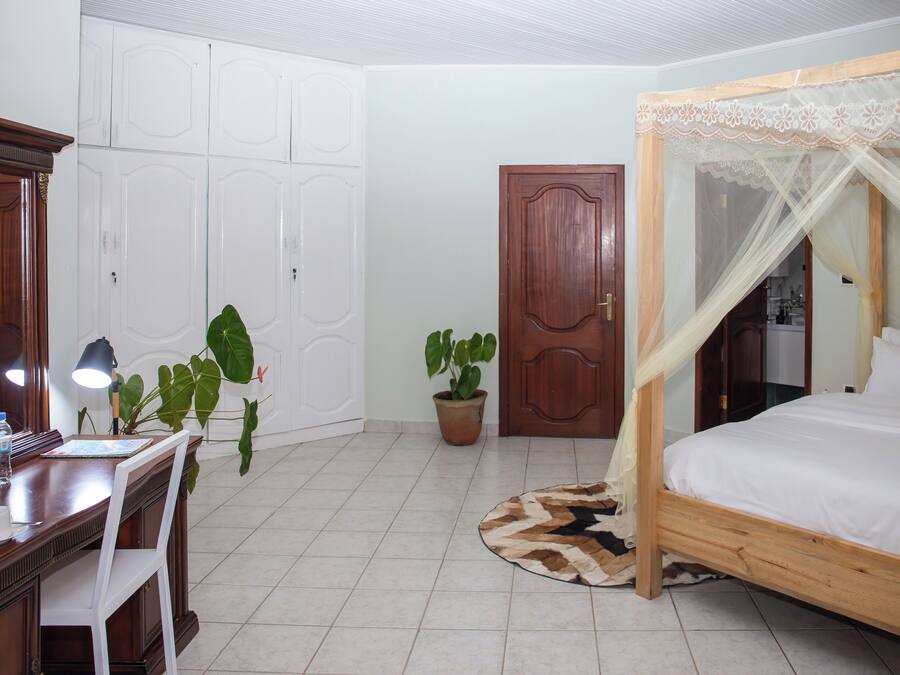A bedroom with a wooden bed, a desk with a chair, a potted plant, a wardrobe, and a door.