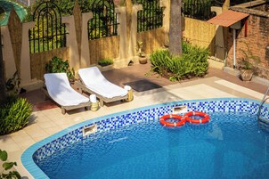 A swimming pool with two sun loungers, a bamboo fence, and a brick wall.