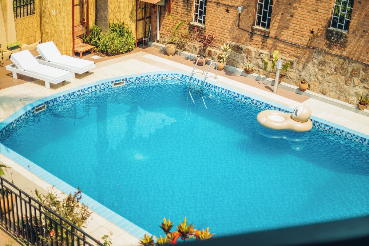 A swimming pool with lounge chairs and an inflatable ring, surrounded by potted plants and a brick wall.