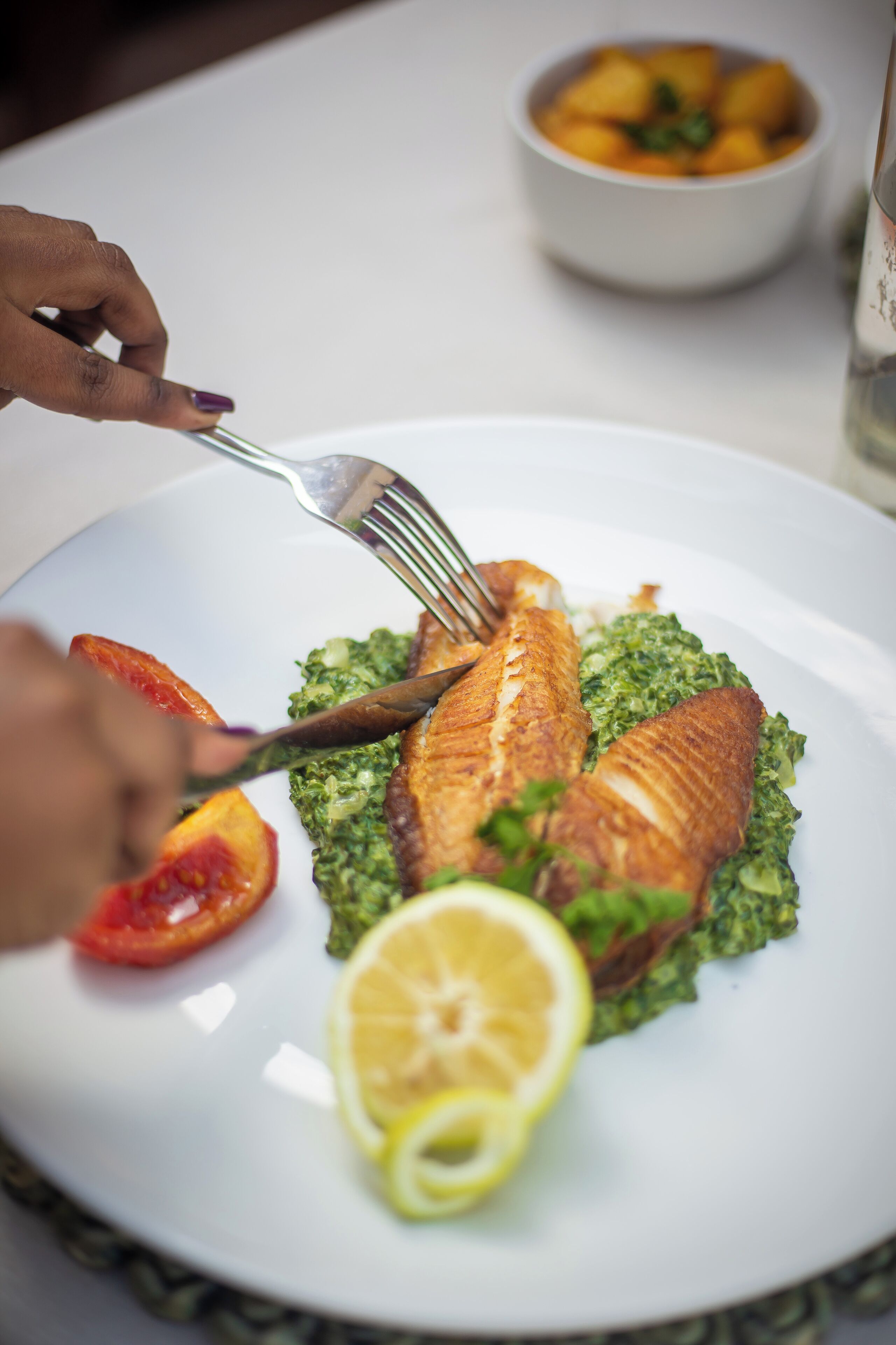 A plate with fish, lemon, and tomato on a white table.
