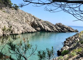 Una costa rocosa con agua turquesa cristalina, vegetación escasa y cielo despejado.