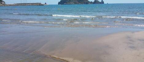 A beach with clear water, a sandy shore, and a distant rocky island.