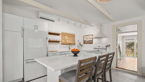 A modern kitchen with white cabinetry, a central island, and a dining area with wooden chairs. - Walk to Downtown - Luxe Backyard - Private + Peaceful Stay (St. Augustine)