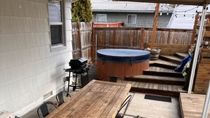 En overdækket terrasse med et træbord og stole, et spabad og en grill.
