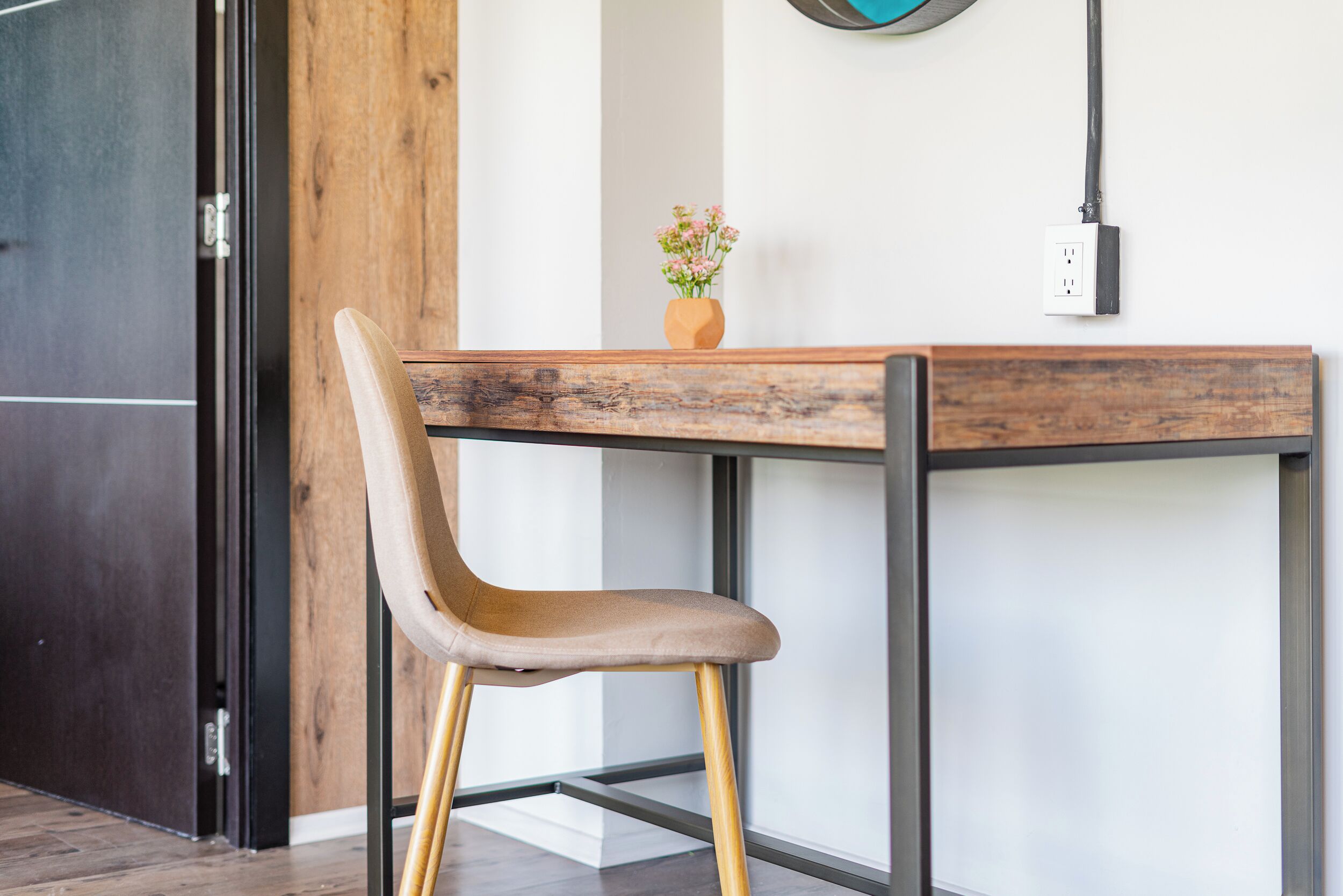 A modern room with a wooden table and a chair, a vase with flowers, and a wall socket.