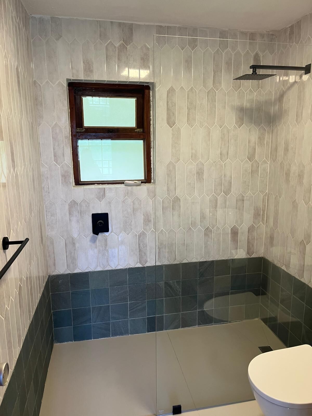 A bathroom with hexagonal patterned tiles, a window, a showerhead, and a toilet.
