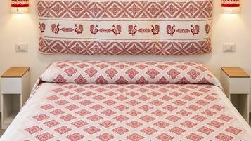 A bedroom with a patterned bedspread, a decorative headboard, and a sunset painting above the bed.