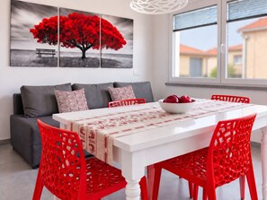 A modern dining area with a white table, red chairs, and a bowl of fruit. - Room-private RED Apartment at Palma de S (Sant'Antioco)
