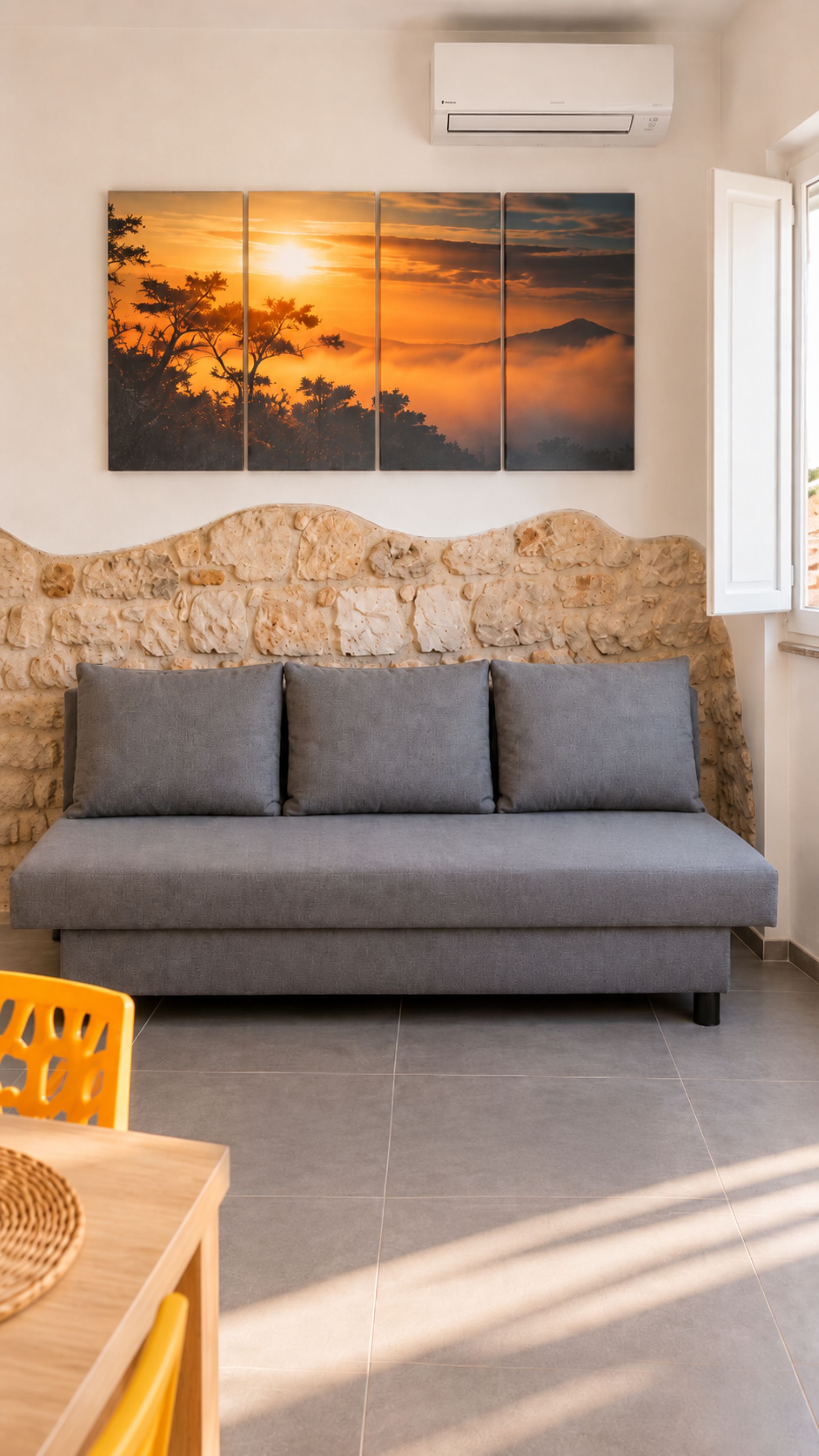 A room with a grey sofa, a stone wall, and a sunset painting.