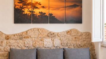 A room with a grey sofa, a stone wall, and a sunset painting.