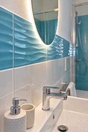 A bathroom with a modern sink, a mirror, and a shower area. - Room-private Blue Apartment at Palma de (Sant'Antioco)