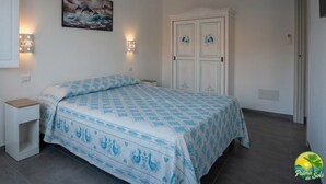 A bedroom with a bed, two bedside tables, a wall-mounted painting, and a wardrobe. - Room-private Blue Apartment at Palma de (Sant'Antioco)