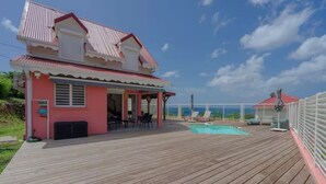 Une maison rose avec une piscine et une terrasse.