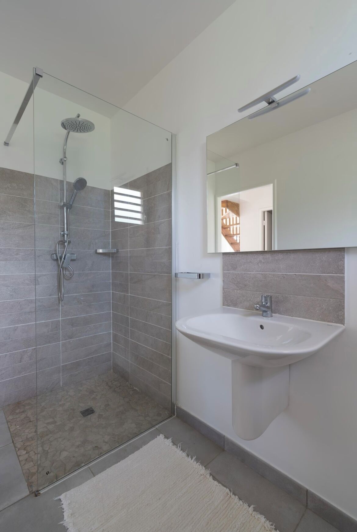 Un baño moderno con ducha de mampara de vidrio, un lavamanos blanco y un espejo grande.