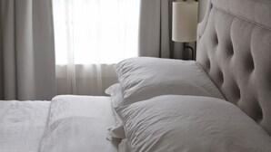 Een net opgemaakt bed met witte lakens, een gestoffeerd hoofdbord en een bedlampje.