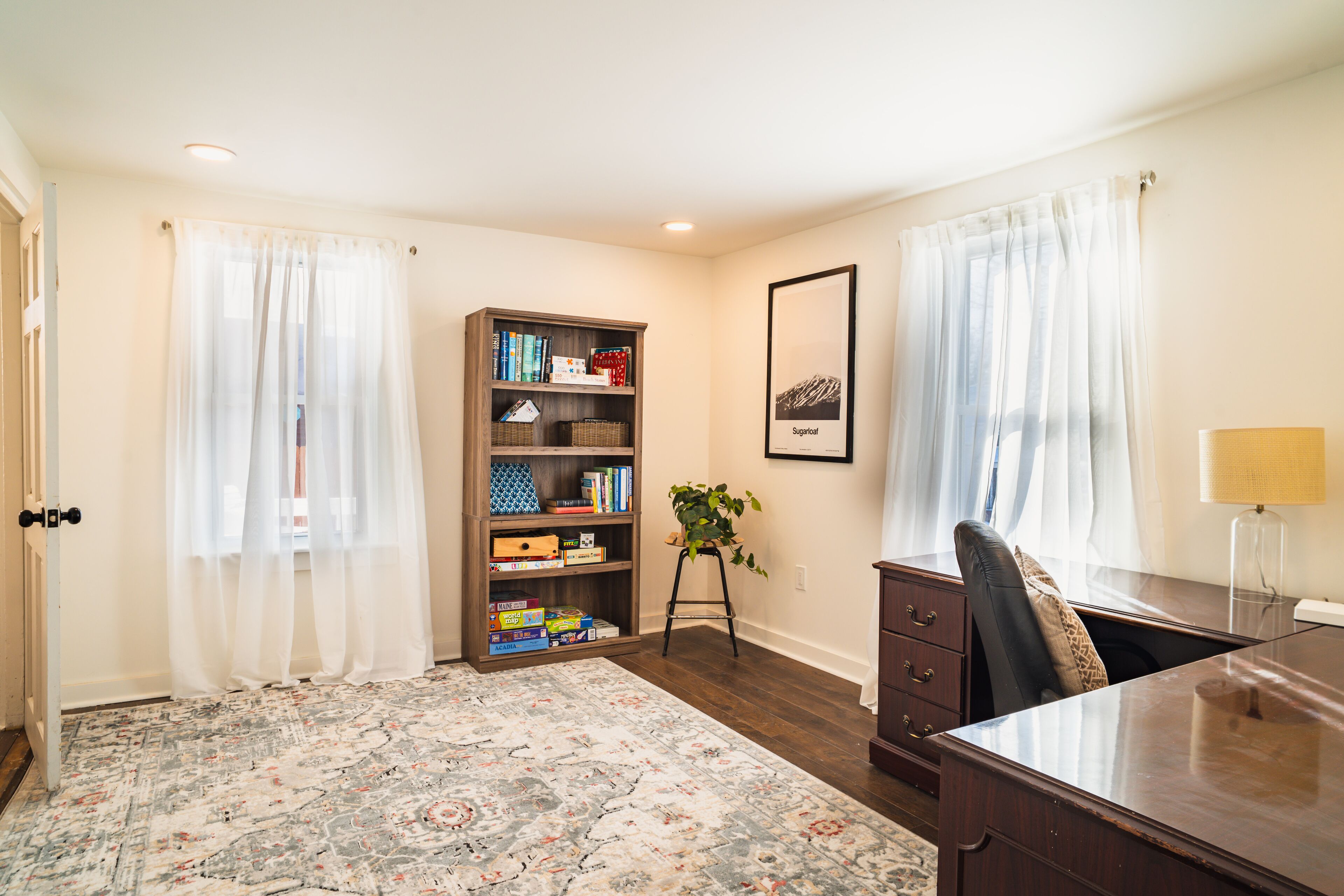 A room with a large bed, a desk, a bookshelf, and a framed picture on the wall.