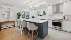 Una cucina moderna con isola centrale, sgabelli da bar, forno integrato e illuminazione a sospensione.