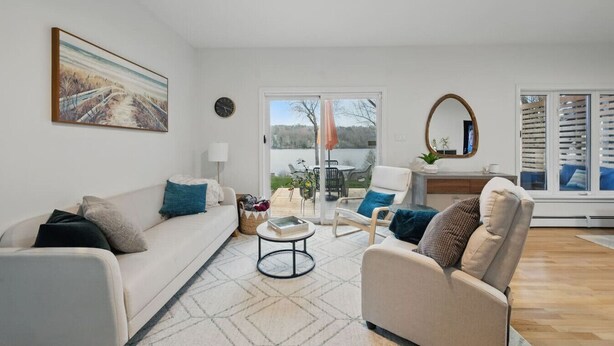 A living room with a white sofa, beige armchairs, a coffee table, and a view of a lake through large glass doors. - The Tranquil lake-house at Fletchers Lake (Fall River)