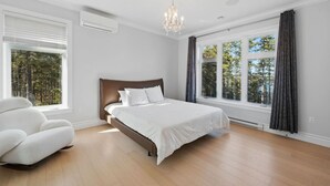 A bedroom with a bed, a chair, a chandelier, and large windows. - Peaceful Retreat on Schmidt Lake (Hammonds Plains)