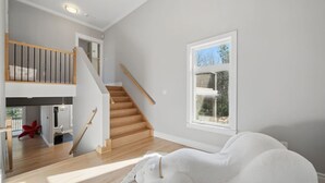 A spacious room with a wooden staircase, a large window with a view, and a plush white sofa. - Peaceful Retreat on Schmidt Lake (Hammonds Plains)