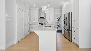 A modern kitchen with white cabinetry, a central island, stainless steel appliances, and a pendant light. - Peaceful Retreat on Schmidt Lake (Hammonds Plains)