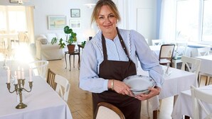 Ein Essbereich mit gedeckten Tischen, ein Kellner mit Tellern und eine Zimmerpflanze im Hintergrund.