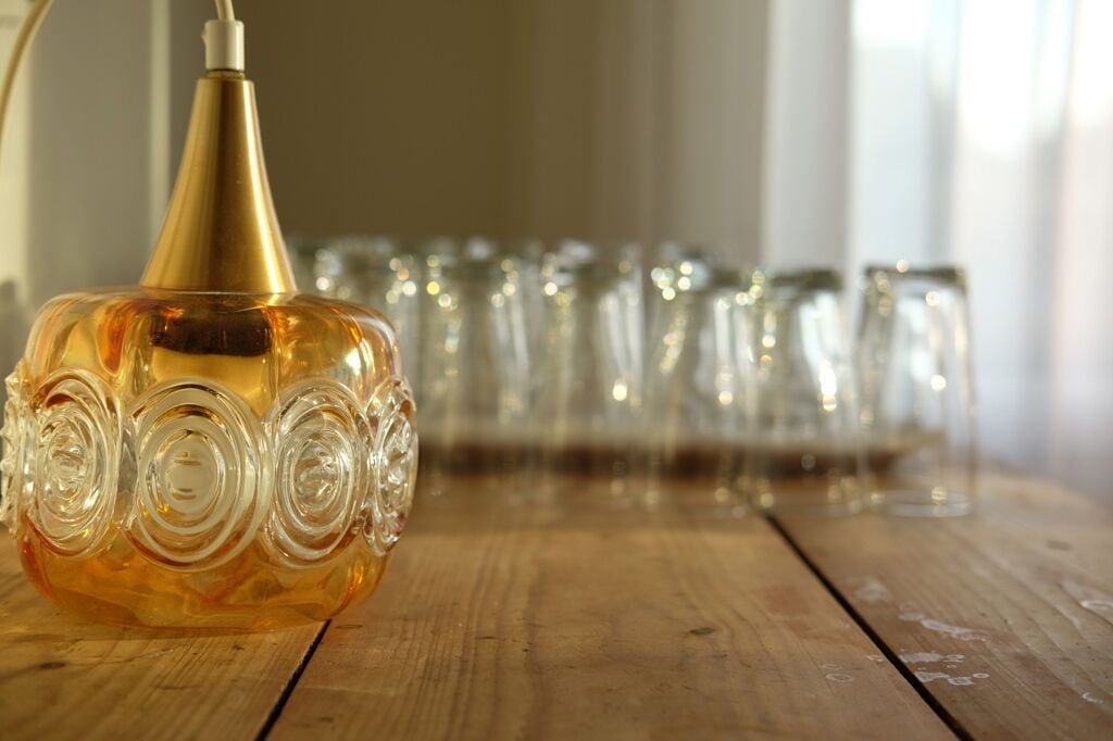 Un ampolla de perfum de vidre sobre una taula de fusta, amb diversos vasos de cristall al fons.