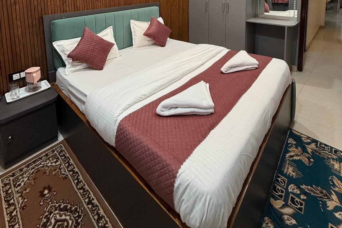 A hotel room with a neatly made bed, a bedside table with a lamp, a wardrobe, and a mirror.